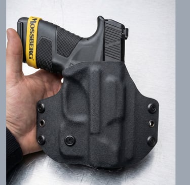 Hand holding a black Mossberg MC2c pistol secured in a custom black Kydex OWB holster.