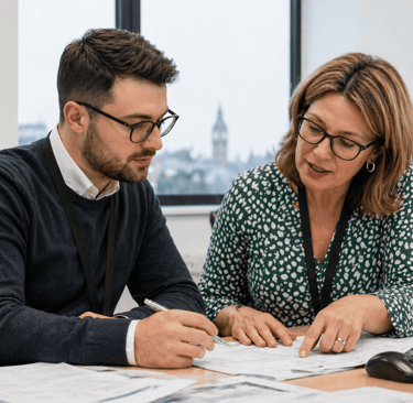 Two colleagues collaborate at a desk with documents.