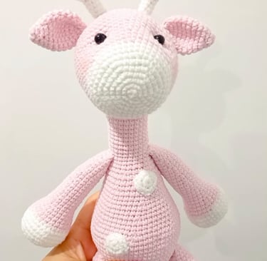 Handmade pink and white amigurumi giraffe crochet plush toy for nursery decor.