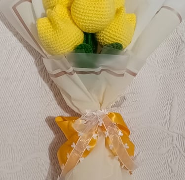 Handmade bouquet of yellow crochet tulips wrapped in white paper with a decorative ribbon bow.
