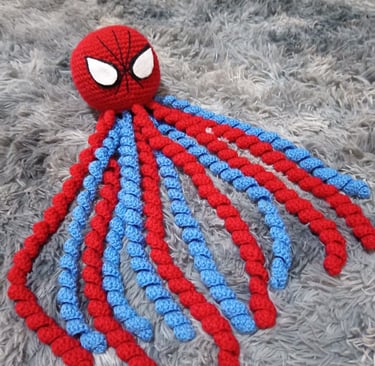 Handmade Spider-Man crochet octopus plush with red and blue curly tentacles on a grey shag rug.