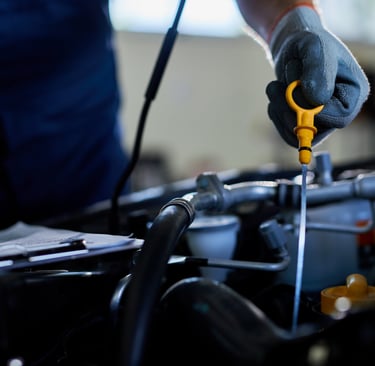 A mechanic holding a yellow dipstick to check engine oil levels during a professional car service.
