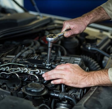 Professional auto mechanic using a socket wrench to perform engine repair and maintenance services on a vehicle.