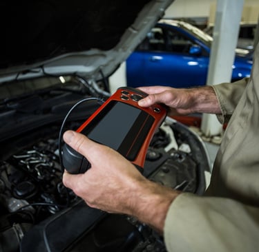 a man in a car engine with a OBD-II tester in his hand
