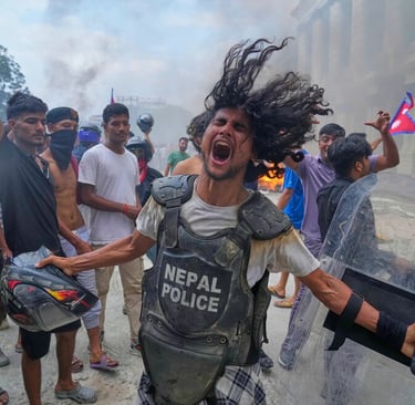 A protester in Nepal shouting and holding a police shield amidst smoke and a crowd during a demonstration.