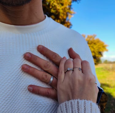 A close-up of a couple's hands with engagement and wedding rings outdoors during autumn.