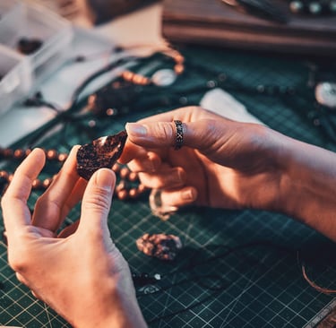 Manos de artesana seleccionando piedras naturales sobre mesa de trabajo para joyería artesanal.