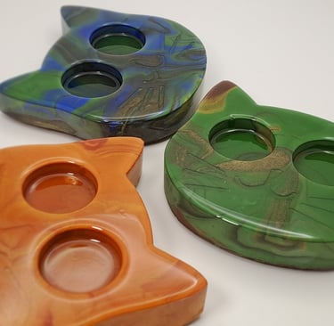 Three cat-shaped gypsum and resin tea light holders in marbled orange, green, and blue patterns.