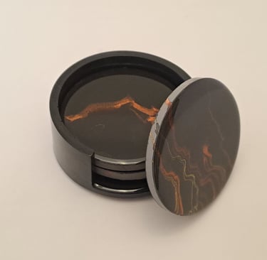 Handcrafted dark coasters in a holder, with black and amber marbled coaster propped up to show its p