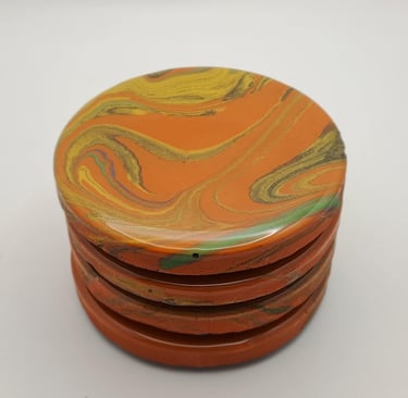 Stacked orange marble resin coasters with swirled yellow and green patterns.