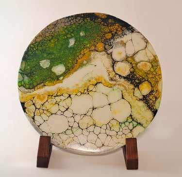 Handcrafted round acrylic pour art piece with green and gold cell patterns on a wooden display stand
