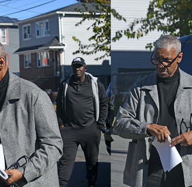 Actor Denzel Washington wearing a grey wool coat and black turtleneck holding a script on a film set.