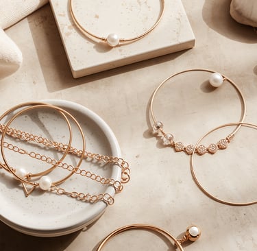 Elegant gold jewelry collection featuring pearl necklaces and minimalist bangle bracelets on a marble surface.
