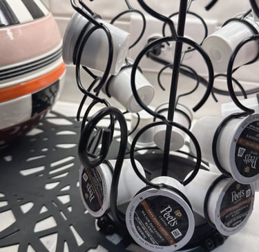 Black wire carousel organizer holding Peet's Coffee K-Cup pods on a white kitchen countertop.