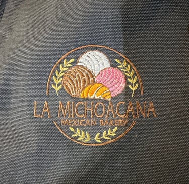 Embroidered logo for La Michoacana Mexican Bakery featuring colorful concha pastries on dark fabric.