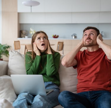 Man and woman cover their ears and look up as they are struggling with noise from upstairs neighbour