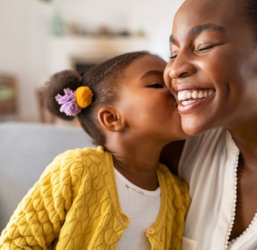 A mother smiles as her young daughter kisses her cheek
