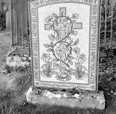Vintage black and white mosaic gravestone in a cemetery with floral designs and a cross.