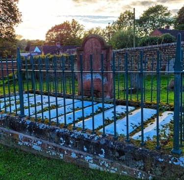 A historic stone grave of The Nine men enclosed by a green iron fence in an old cemetery at sunset.