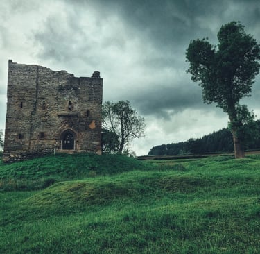 Historic stone castle ruins standing on a green hill under a dramatic cloudy sky.