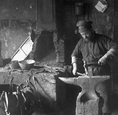 Vintage black and white photo of a blacksmith forging metal on an iron anvil in a traditional forge.