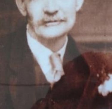 Vintage sepia portrait of an elderly man with a mustache in a formal suit and tie.