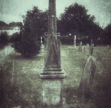 Vintage-style photo of an old stone obelisk monument and headstones in a historic graveyard.