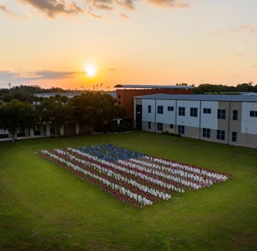 Aerial view of an American flag made of small flags on a school lawn at sunset.