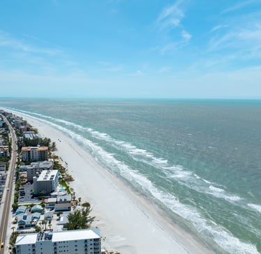 Aerial view of a white sand beach coastline with beachfront hotels and ocean waves.