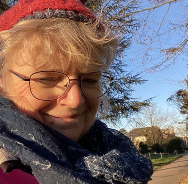 Person mit roter Mütze, Brille und dunkelblauem Schal mit Anker-Muster im Freien an einem sonnigen T