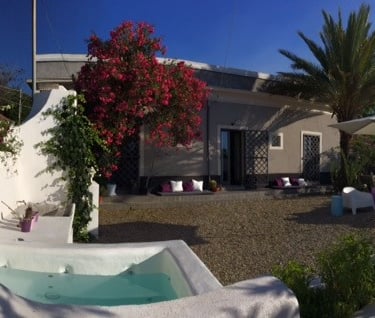 Luxury villa courtyard with a plunge pool, blooming bougainvillea, and palm trees under a blue sky.