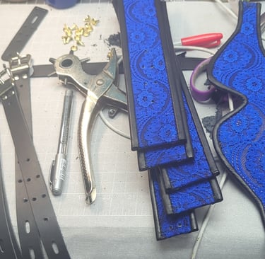 Handmade blue lace lace and leather pieces and eye mask on a workbench with leather crafting tools.