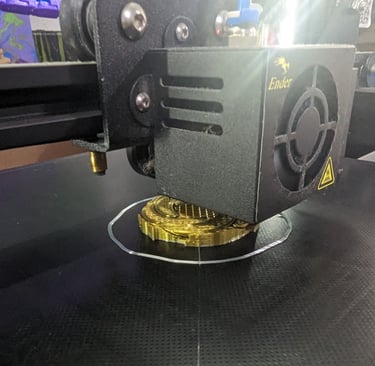 An Ender 3D printer extruding golden silk PLA filament to create a detailed circular model on a black print bed.