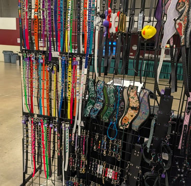 A retail display rack featuring a variety of colorful pet collars, harnesses, and leather accessories.