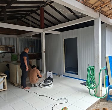 Technicians installing cold storage panel insulation in a white tiled warehouse area.