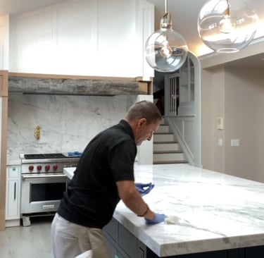 Professional Applicator sealing a white marble kitchen island countertop during a home renovation.