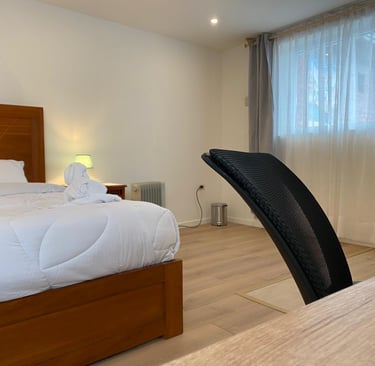 Dormitorio moderno con cama de madera, sábanas blancas y silla de oficina ergonómica para trabajar