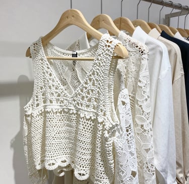 A collection of plus size clothing items displayed on elegant hangers against a beige sand backdrop, emphasizing the brand’s neutral palette.