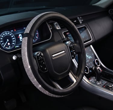 Luxury black leather steering wheel cover with sparkling diamond rhinestones for a car interior.