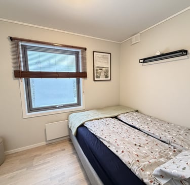 Modern guest bedroom with a twin bed, patterned bedding, neutral walls, and a window with wooden blinds.