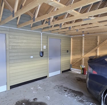 Interior of a modern timber frame carport with a black electric vehicle charging station installed on a wooden wall.