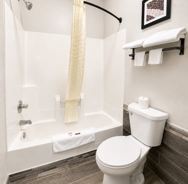 Modern bathroom interior featuring a white bathtub, toilet, and grey wood-look tile floors.