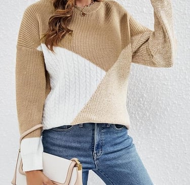 Woman wearing a tan and white colorblock cable knit sweater with blue denim jeans.