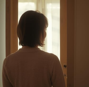 Back view of a woman with short brown hair looking through a doorway toward a bright light.