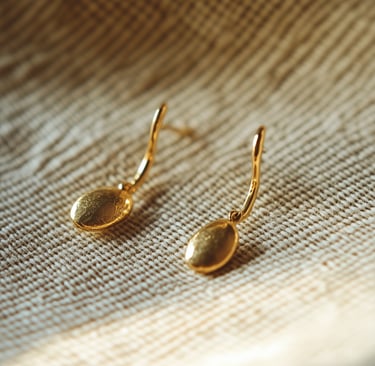 Elegant gold drop earrings with a textured oval design on a neutral linen fabric background.