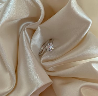 Elegant round-cut diamond engagement ring nestled in folds of ivory silk fabric.