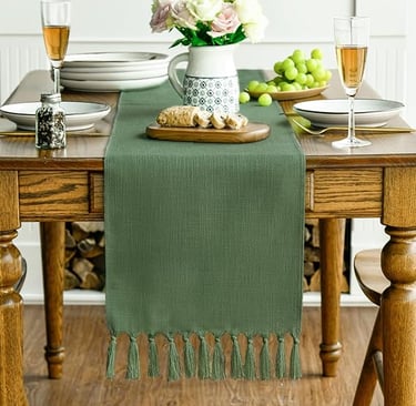 Green boho table runner with textured fringe detail, displayed on a natural wooden dining table.