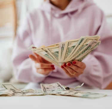 A woman in a pink hoodie, sitting at a tble and counting money.