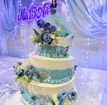 Pastel de quinceañera azul claro y blanco de tres niveles decorado con rosas, mariposas y un adorno 