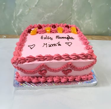Pastel de cumpleaños cuadrado helado rosa con escritura Feliz Cumple Mamá y adornos de frutas en una